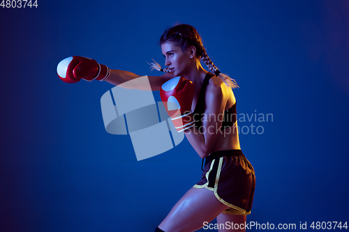 Image of Fit caucasian woman in sportswear boxing on blue studio background in neon light