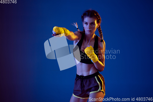 Image of Fit caucasian woman in sportswear boxing on blue studio background in neon light