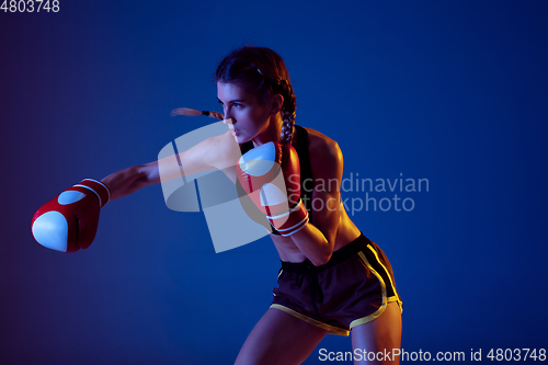 Image of Fit caucasian woman in sportswear boxing on blue studio background in neon light