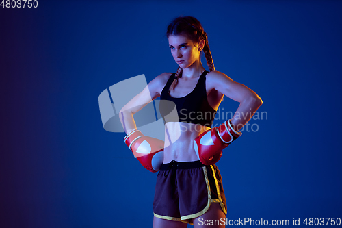 Image of Fit caucasian woman in sportswear boxing on blue studio background in neon light