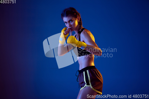 Image of Fit caucasian woman in sportswear boxing on blue studio background in neon light