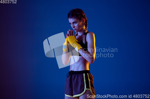 Image of Fit caucasian woman in sportswear boxing on blue studio background in neon light