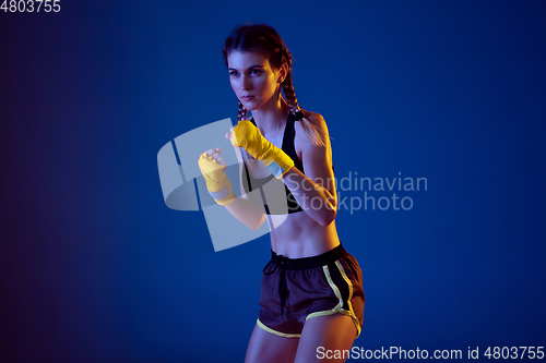 Image of Fit caucasian woman in sportswear boxing on blue studio background in neon light