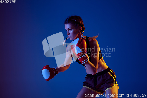 Image of Fit caucasian woman in sportswear boxing on blue studio background in neon light