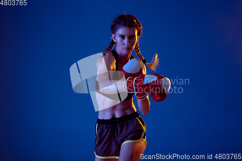Image of Fit caucasian woman in sportswear boxing on blue studio background in neon light