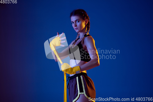 Image of Fit caucasian woman in sportswear boxing on blue studio background in neon light