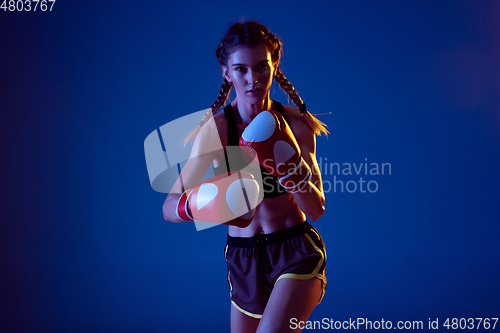 Image of Fit caucasian woman in sportswear boxing on blue studio background in neon light