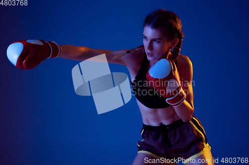 Image of Fit caucasian woman in sportswear boxing on blue studio background in neon light