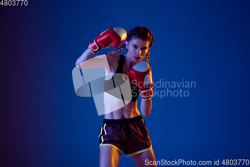 Image of Fit caucasian woman in sportswear boxing on blue studio background in neon light
