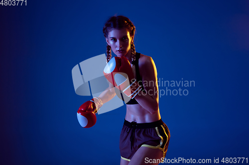 Image of Fit caucasian woman in sportswear boxing on blue studio background in neon light