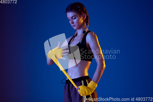 Image of Fit caucasian woman in sportswear boxing on blue studio background in neon light