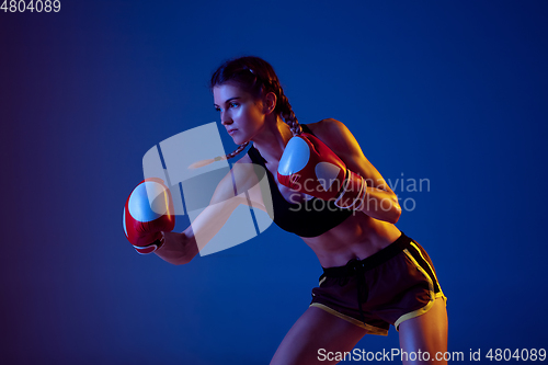 Image of Fit caucasian woman in sportswear boxing on blue studio background in neon light