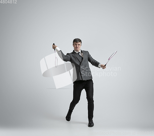 Image of Caucasian man in office clothes plays badminton isolated on grey studio background