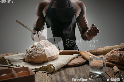 Image of Close up of african-american man slices fresh bread with a kitchen knife