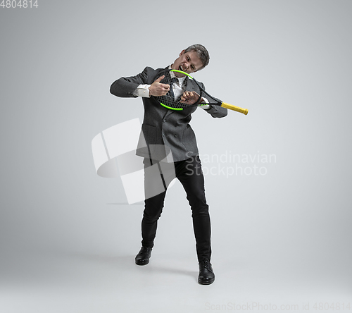 Image of Caucasian man in office clothes plays tennis isolated on grey studio background