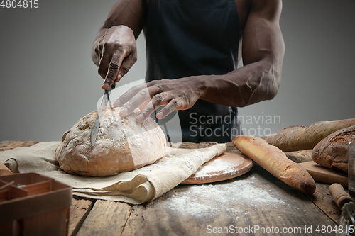 Image of Close up of african-american man slices fresh bread with a kitchen knife