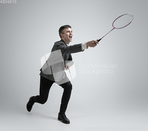 Image of Caucasian man in office clothes plays badminton isolated on grey studio background