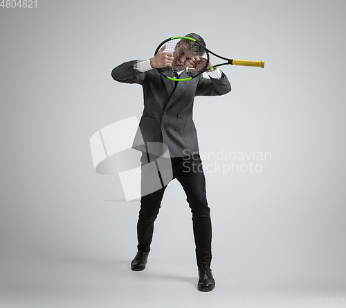 Image of Caucasian man in office clothes plays tennis isolated on grey studio background