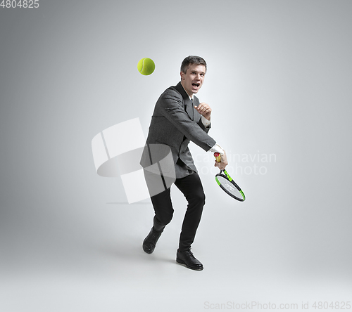 Image of Caucasian man in office clothes plays tennis isolated on grey studio background