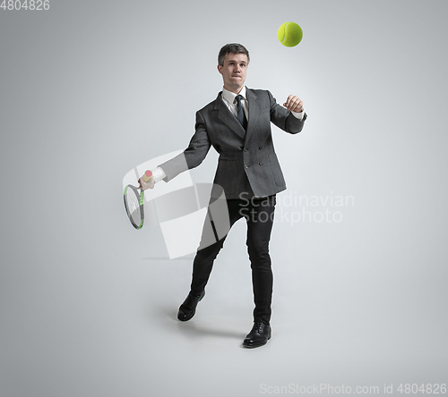 Image of Caucasian man in office clothes plays tennis isolated on grey studio background