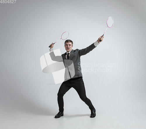 Image of Caucasian man in office clothes plays badminton isolated on grey studio background