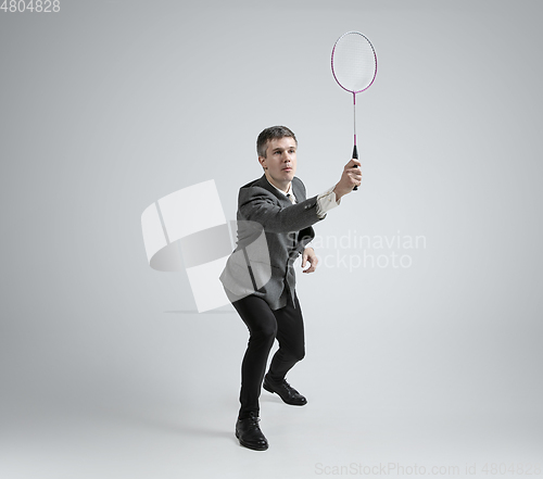 Image of Caucasian man in office clothes plays badminton isolated on grey studio background