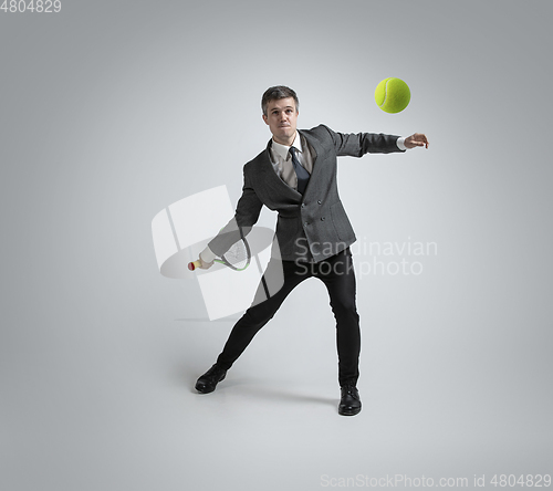 Image of Caucasian man in office clothes plays tennis isolated on grey studio background