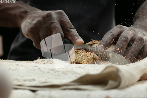 Image of Close up of african-american man slices fresh bread with a kitchen knife