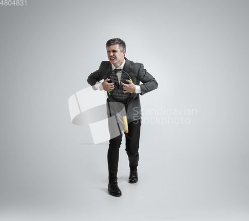 Image of Caucasian man in office clothes plays tennis isolated on grey studio background