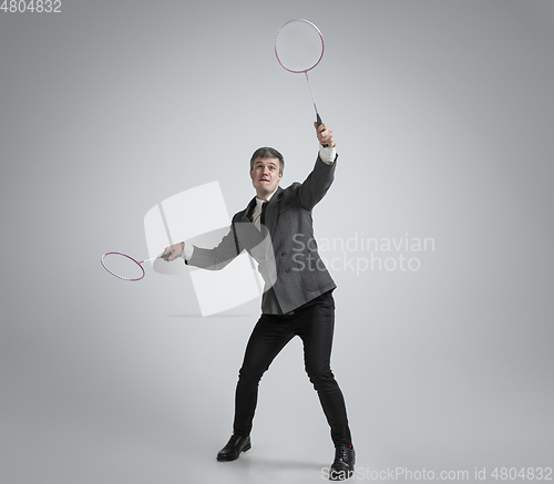 Image of Caucasian man in office clothes plays badminton isolated on grey studio background