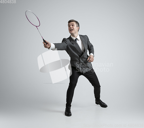 Image of Caucasian man in office clothes plays badminton isolated on grey studio background