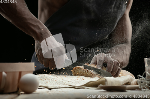 Image of Close up of african-american man slices fresh bread with a kitchen knife