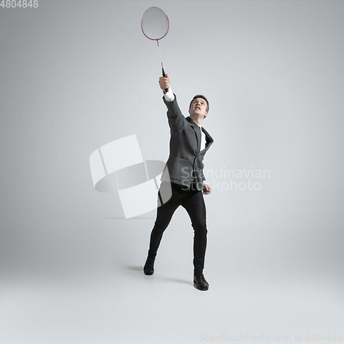 Image of Caucasian man in office clothes plays badminton isolated on grey studio background