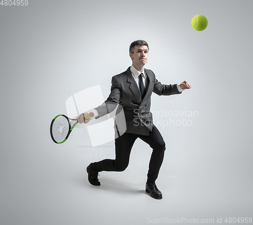 Image of Caucasian man in office clothes plays tennis isolated on grey studio background