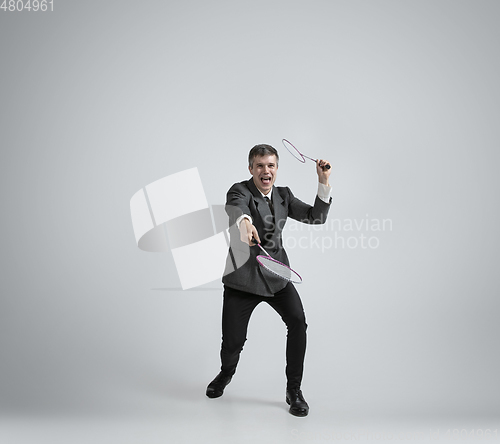 Image of Caucasian man in office clothes plays badminton isolated on grey studio background