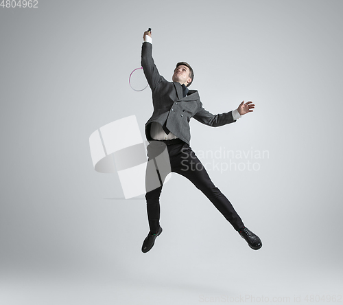 Image of Caucasian man in office clothes plays badminton isolated on grey studio background