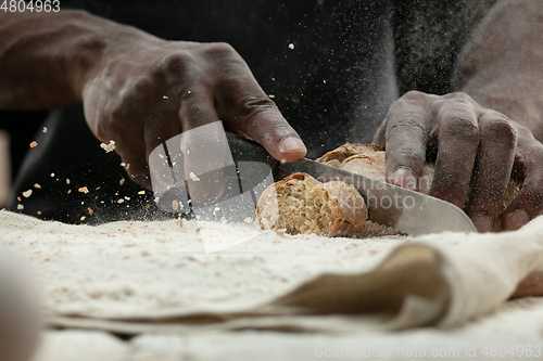 Image of Close up of african-american man slices fresh bread with a kitchen knife