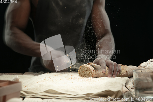 Image of Close up of african-american man slices fresh bread with a kitchen knife