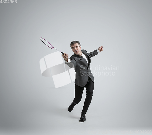 Image of Caucasian man in office clothes plays badminton isolated on grey studio background