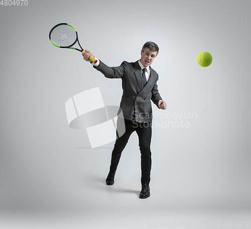 Image of Caucasian man in office clothes plays tennis isolated on grey studio background