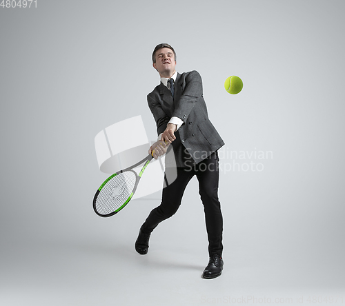 Image of Caucasian man in office clothes plays tennis isolated on grey studio background