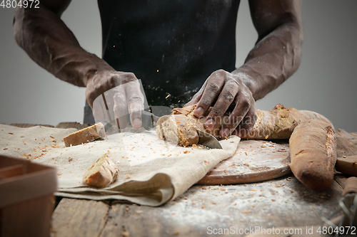 Image of Close up of african-american man slices fresh bread with a kitchen knife