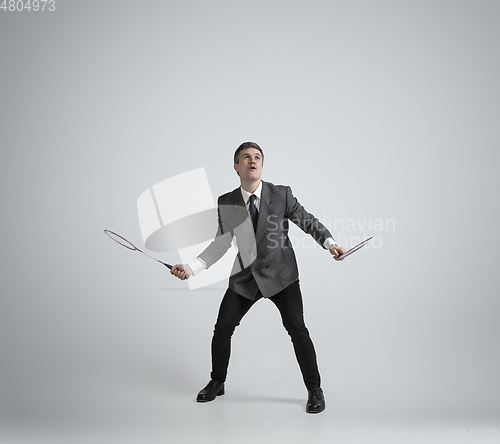 Image of Caucasian man in office clothes plays badminton isolated on grey studio background