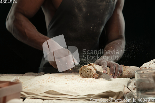 Image of Close up of african-american man slices fresh bread with a kitchen knife