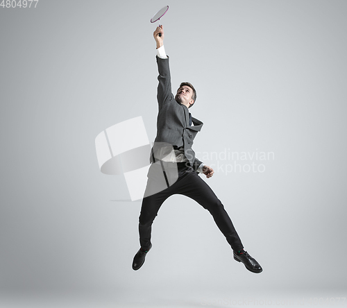 Image of Caucasian man in office clothes plays badminton isolated on grey studio background