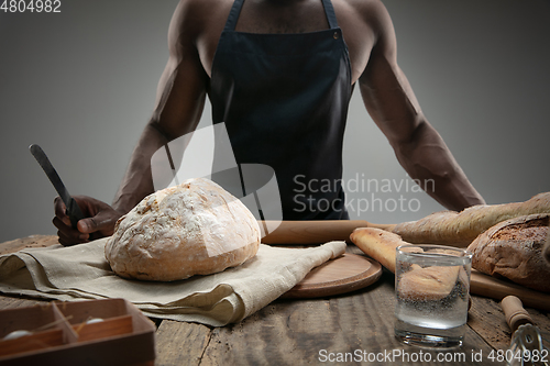 Image of Close up of african-american man slices fresh bread with a kitchen knife