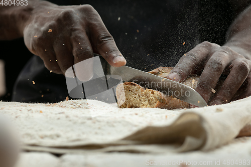 Image of Close up of african-american man slices fresh bread with a kitchen knife