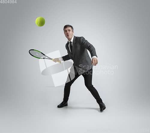 Image of Caucasian man in office clothes plays tennis isolated on grey studio background