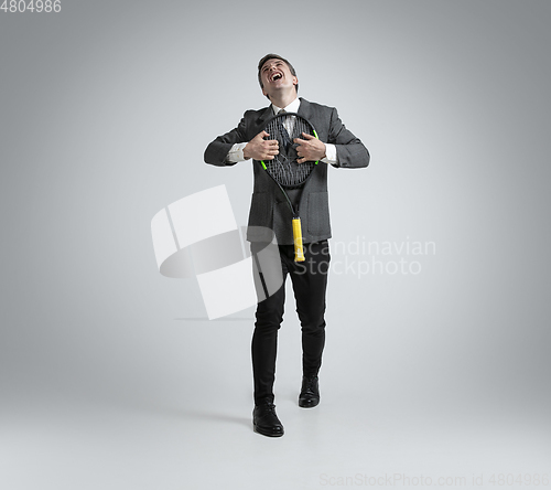 Image of Caucasian man in office clothes plays tennis isolated on grey studio background