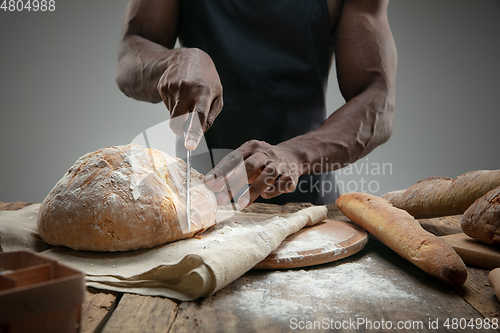 Image of Close up of african-american man slices fresh bread with a kitchen knife